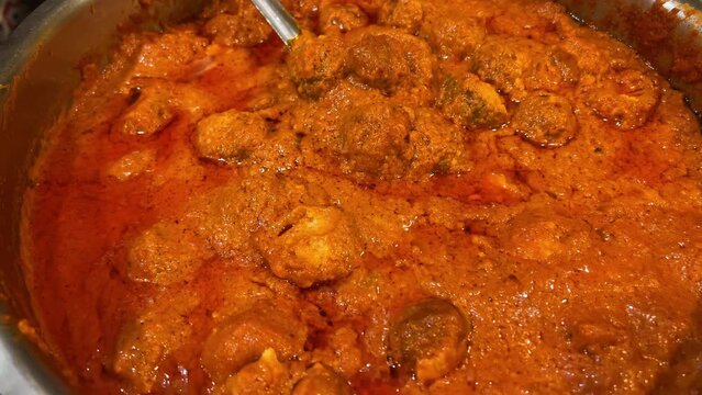 Indian cuisine - Cinematic shot of Kashmiri aloo kofta made of potatoes in red gravy in a metal bowl.