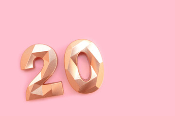 Gold colored number twenty on a pink background with copy space.