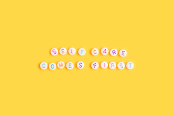 Self care comes first. Quote made of white round beads with multicolored letters on a yellow...