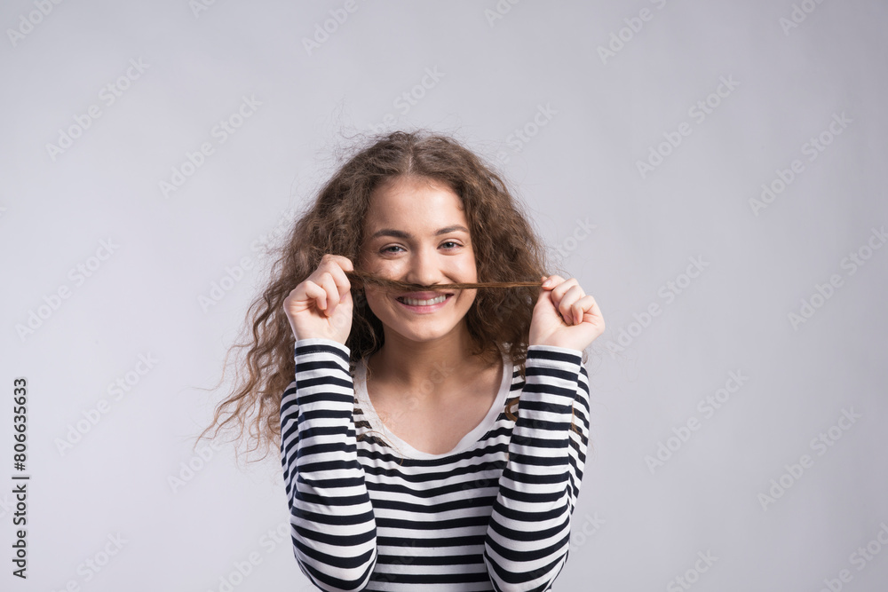 Wall mural portrait of a gorgeous teenage girl with curly hair, holding lock of hair as a moustache. studio sho