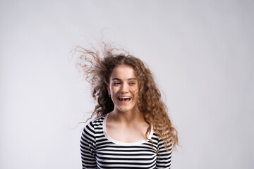 Portrait of a gorgeous teenage girl with curly hair, blowing in wind. Studio shot, white background...