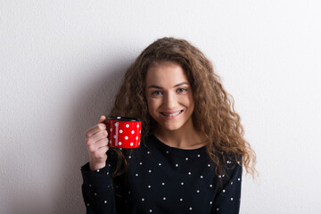 Portrait of a gorgeous teenage girl with curly hair drinking tea from mug. Studio shot, white...