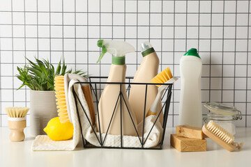 Basket with towel and bottles of detergents, brushes and plant on light background