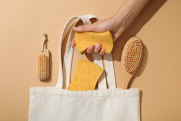 Brushes in cotton bag and sponges in hand on beige background, top view