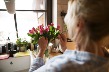 Beautiful mature woman arranging bouquet of roses in a vase, a hobby and relaxation. Older woman...