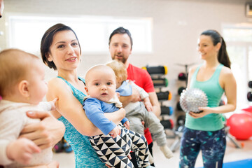 Group exercise class, parents working out with baby in gym. Moms and dad staying active while...