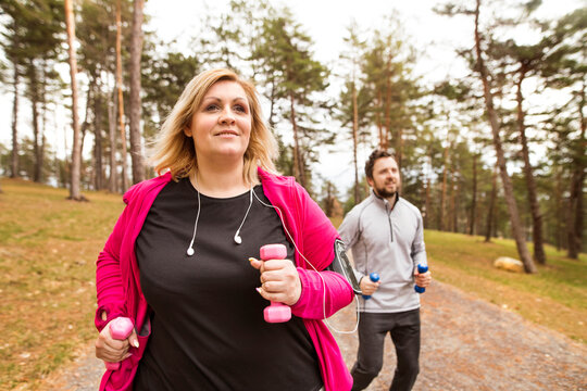 An overweight woman running in nature with friend. Exercising outdoors for people with obesity, support from friend, fitness coach.