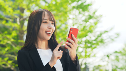 新緑を背景にスマホを使う女性ビジネスパーソン