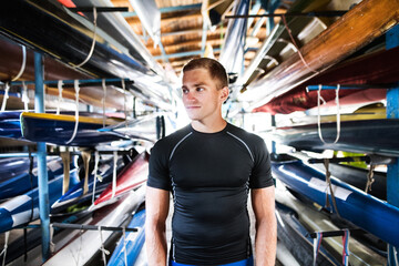 Portrat of young canoeist standing in the middle of stacked canoes. Concept of canoeing as dynamic...
