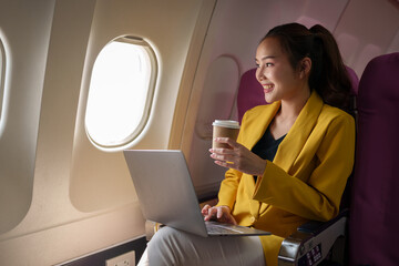 Attractive Asian female passenger on airplane sitting in comfortable seat holding glass of hot...