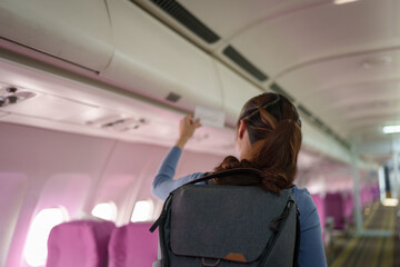 Confident Asian female traveler traveling by plane A passenger carrying a backpack and boarding pass searches for her seat number on a plane traveling abroad.