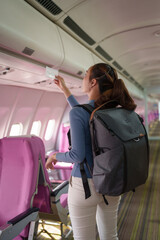 Confident Asian female traveler traveling by plane A passenger carrying a backpack and boarding pass searches for her seat number on a plane traveling abroad.