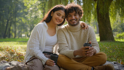 Happy smiling multiethnic couple in love african american indian man woman having picnic on blanket park outdoors boyfriend girlfriend guy girl enjoy coffee romantic date together hug posing in nature