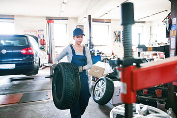 Female auto mechanic changing tieres in auto service. Beautiful woman holding tire in a garage,...