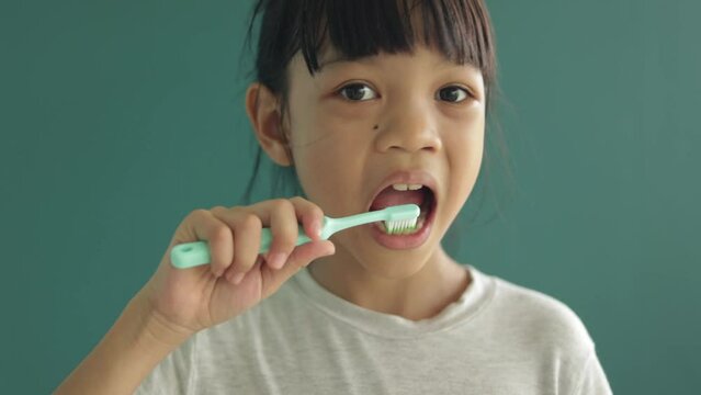 Cute kid girl, elementary school age Demonstrating how to clean teeth use a toothbrush that is the right size for her age. and Brush all over the mouth. for have good dental health. green background.