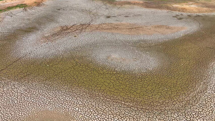 From above, a drone captures the desolation of parched land, its cracked surface stretching endlessly, punctuated only by sparse green patches-a stark portrayal of drought's relentless grip.
