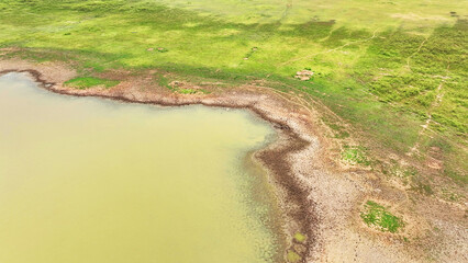 Aerial vista reveals parched earth and sparse vegetation in a drought-stricken dam, showcasing the...
