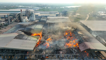 Massive industrial structure consumed by relentless blaze. Fiery tongues lick at crumbled sections,...