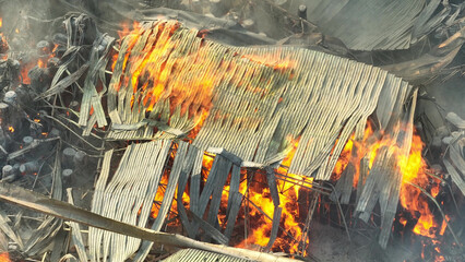 A raging inferno consumes the industrial site, fierce flames dancing amidst mangled metal. Thick...