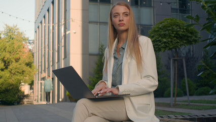 Pensive Caucasian woman businesswoman student female business lady girl developer think typing on laptop outdoors street near office work remote online thinking pondering idea journalist write article
