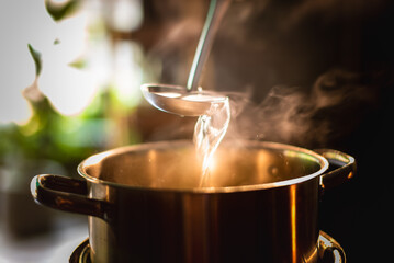 A boiling pot steams up as a restaurant's chef uses a ladle to stir soup in a cooking pot in the...
