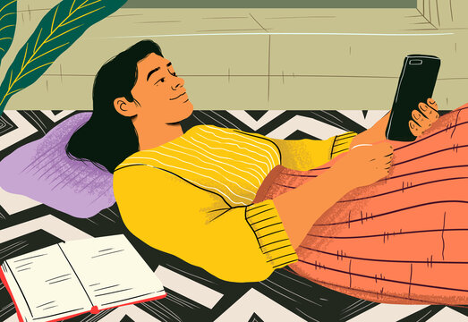 Content woman using mobile phone lying by notebook on patterned rug