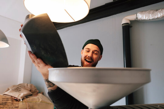 Happy coffee roaster pouring raw coffee beans in machine