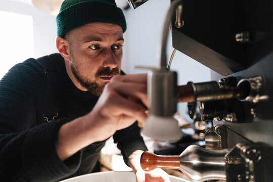 Coffee roaster wearing knit hat and operating machinery in factory