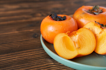 Ripe persimmon on a plate on a wooden background.