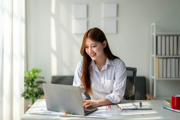 A woman is sitting at a desk with a laptop in front of her. She is smiling and she is enjoying her work