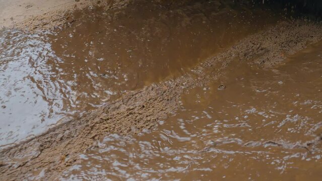 Car drives through puddle, splashing water and mud in different directions. Spinning SUV tires close-up. Rotating tyre on dirty road. Automobile offroad