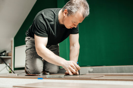 Kneeling man marking laminate panel on floor at home