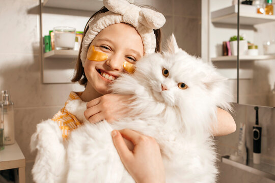 Smiling girl with eye gel pack carrying white cat in bathroom