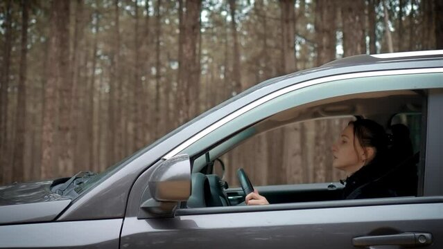 Woman practicing driving car, cruising along deserted forest trail with no traffic around, independently hones driving skills. Female learn driving and traveling alone. Shooting from outside