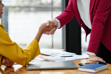 Two businesswomen hold hands on a table while finishing a work briefing. An agreement or...