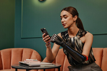 Confident young businesswoman with prosthetic arm using smart phone sitting on sofa in office