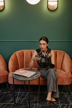 Confident businesswoman with prosthetic arm using smart phone sitting on sofa in office