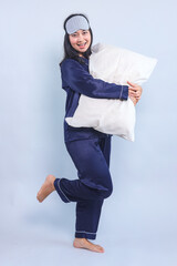 Full body of woman in pajamas and sleep eye mask holding and hugging pillow