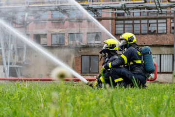 Two firefighters use a stream of water from a hose to cool a tank of highly flammable liquid at a chemical factory