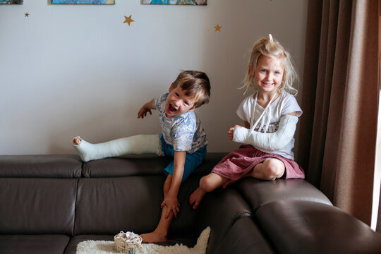 Siblings with broken body parts sitting on couch at home