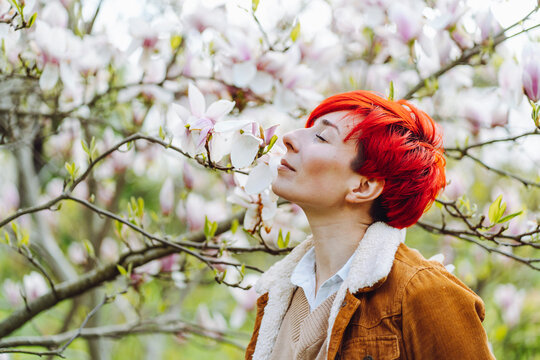 Beautiful redhead woman eyes closed smelling magnolia blossom in park