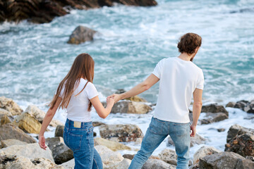 Man and Woman Holding Hands Walking on Rocks by the Ocean