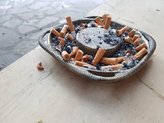 Cigarette butts in ashtray on wooden table.