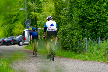Obraz premium Adult couple of racing cyclists surrounded by bushes on a rural road at Swiss City of Zürich on a spring day. Photo taken May 5th, 2024, Zurich, Switzerland.
