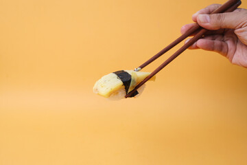 Chopsticks hold egg sushi or tamago sushi. Japanese tradition food isolated on yellow background.