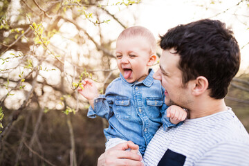 Portrait of father holding little toddler boy, showing him buds on twig. Family time oudroor during...