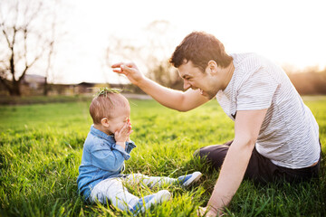 Father playing with little toddler boy in grass, having fun during warm spring day. Father's day concept.