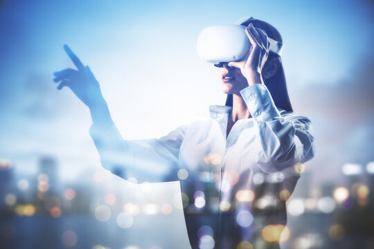 Attractive young european businesswoman with VR glasses standing on blurry airy city background with mock up place. Future, tomorrow and virtual reality concept. Double exposure. - Powered by Adobe