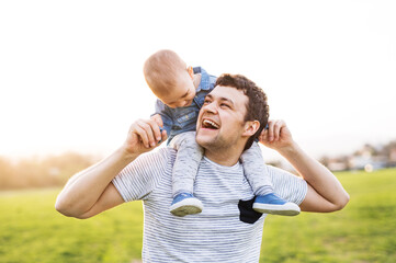 Father carrying little toddler on shoulders, having fun during warm spring day. Father's day...