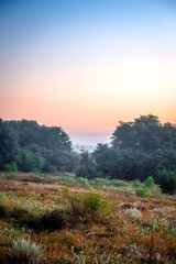 Red sunrise over the field with trees and forest . Morning at summer . Fog over the field and trees . Beautiful landsapes . Red sky and blue hour on nature . Smoothly foggy morning 